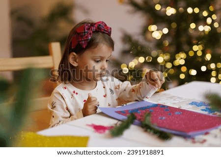 
Merry Christmas and happy holidays. Adorable little kid make cards, gifts and decorations for the holiday. Cute toddler girl doing creativity. Girl getting ready for christmas.