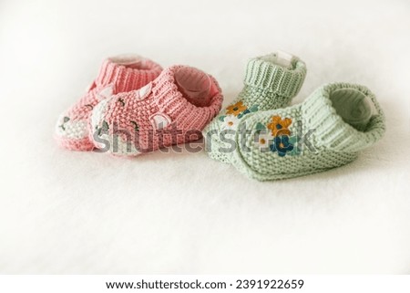 Pink and green knitted children's shoes on a white background with copy space. Pregnancy and motherhood concept, first birthday banner, handmade socks, baby warm clothes, handmade knitted socks. Royalty-Free Stock Photo #2391922659