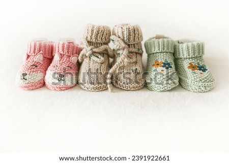 Three pairs of children's shoes on a white background with copy space. Pregnancy and motherhood concept, first birthday banner, handmade socks, baby warm clothes, handmade knitted socks. Royalty-Free Stock Photo #2391922661