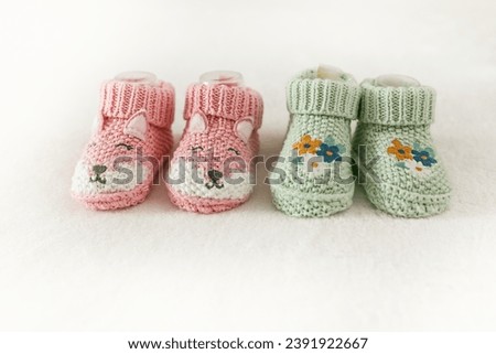 Two pairs of children's shoes on a white background with copy space. Pregnancy and motherhood concept, first birthday banner, handmade socks, baby warm clothes, handmade knitted socks. Royalty-Free Stock Photo #2391922667