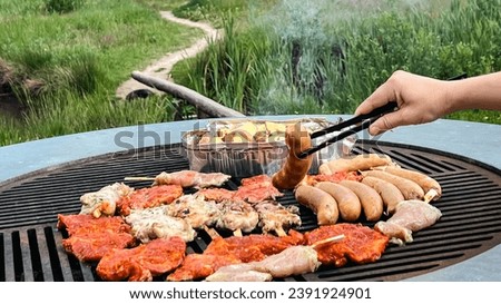 Woman having a picnic barbeque grill in the garden and doing steaks and sausage on a grill. Summer party outdoors, roasted meat, sausage, pork, spicy meat, traditional barbecue.