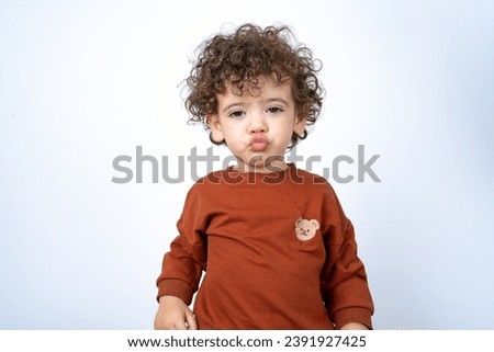 Beautiful two year old toddler with curly hair wearing casual clothes over white studio background blowing kiss to his mother. 