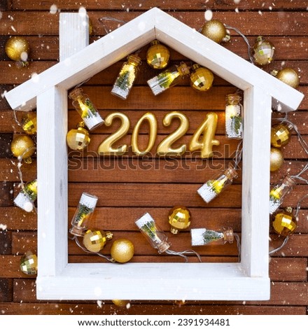 House key with keychain cottage on festive brown wooden background with stars, lights of garlands. New Year 2024 wooden letters, greeting card. Purchase, construction, relocation, mortgage, insurance
