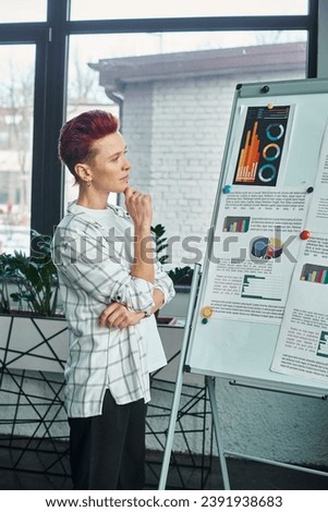 thoughtful bigender person looking at flip chart with business analytics in while working in office