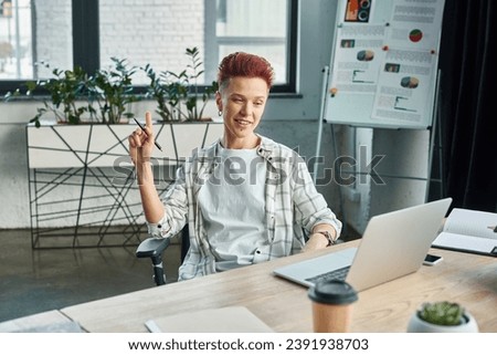 creative bigender manager sitting at workplace near laptop and showing idea sign in office