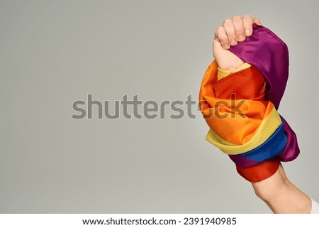 cropped view of hand of non-binary person holding LGBT flag on grey backdrop with copy space