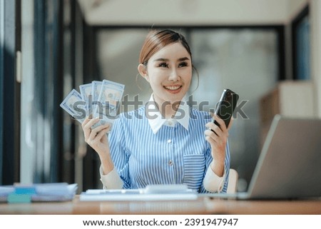 Happy beautiful Asian businesswoman holding money in hand Smartphone and laptop on table in office investment ideas success in business