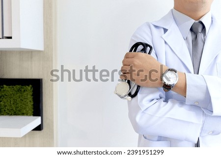 Confident male doctor in white workwear lab coat holding stethoscope standing with arms crossed in corridor of medical clinic, doctor working at hospital. medical and health care concept.