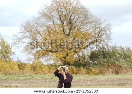 Fashion look, pretty cool young man with retro film camera wearing a elegant sweater outdoors over rural fall background. Design. Photographer or blogger.