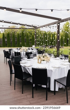 Black chairs and tables decorated white white plates and natural purple and white flowers and reed, candles and gold frames. Wedding decoration and decor, floristic concept