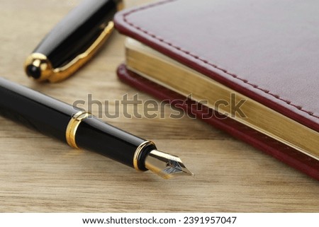 Stylish fountain pen, cap and notebook on wooden table, closeup Royalty-Free Stock Photo #2391957047