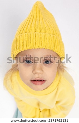 Portrait of beautiful cute little toddler girl. Child with funny face in yellow sweatshirt and yellow hat. Pretty smile kid in studio on white background. High quality photo