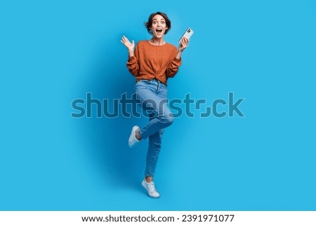 Full size photo of attractive young woman raise hand impressed hold gadget dressed stylish brown clothes isolated on blue color background