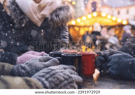 Hands in gloves around steaming mugs of mulled wine at a christmas market, with copyspace for your individual text.