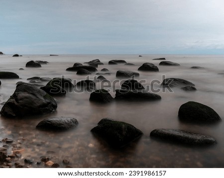 Witness the sea's whispers frozen in time—stones entangled in a mystic embrace, revealed by the haunting beauty of long exposure. Kaltenes Akmenaina Pludmale, Roja, Latvija, Latvia EU