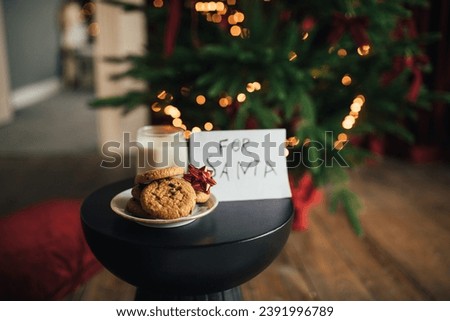 Christmas cookies and milk in a glass for Santa Claus on wooden floor under decorated Christmas tree.