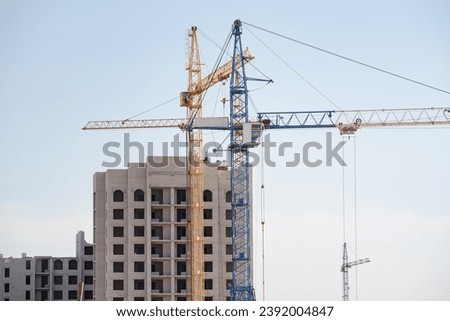 A tower crane builds new houses. The construction process using a tower crane. Construction of residential buildings. Cranes on the construction site. Modern urban planning. Royalty-Free Stock Photo #2392004847