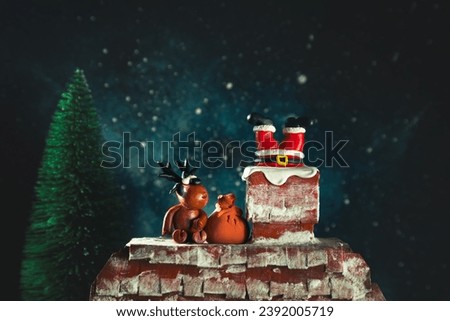 Santa's legs are sticking out of the chimney. Funny plasticine deer sits nearby. Night, starry sky, Christmas background.