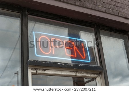neon orange and blue open sign above a grungy door to the entrance of a business