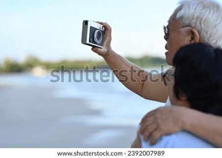 Romantic Senior couple using camera take a picture together on the beach, wedding anniversary and Senior's love concepts.