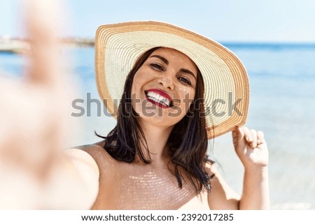 Young beautiful hispanic woman tourist making selfie by the camera at seaside