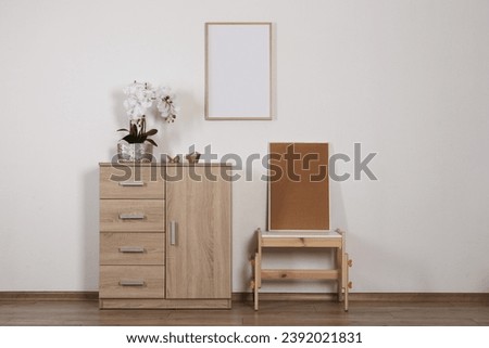 Chest of drawers, table, orchid and picture frames indoors. Interior design
