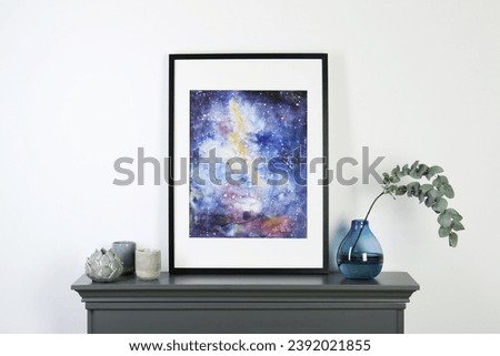 Frame with picture, candles and eucalyptus branch in vase on fireplace near white wall indoors. Interior element