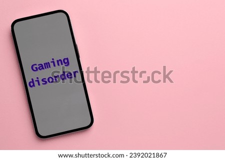 Smartphone with phrase Gaming Disorder on pink background, top view and space for text. Addictive behavior