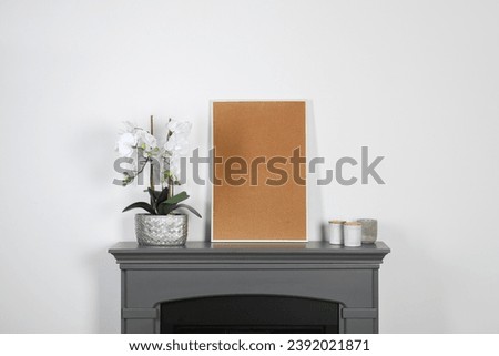 Picture frame, candles and orchid on fireplace near white wall indoors. Interior element
