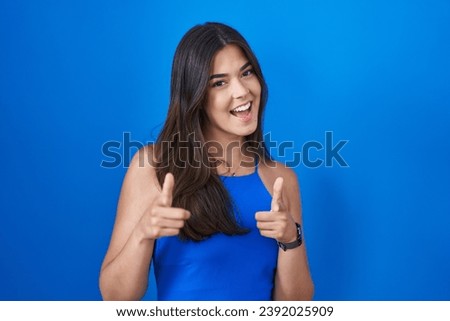 Hispanic woman standing over blue background pointing fingers to camera with happy and funny face. good energy and vibes. 