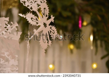 a lot of snowflakes cut out of white paper and hung in garlands. New Year's and Christmas decorations made by hand against the background of garlands with lights and Christmas tree branches