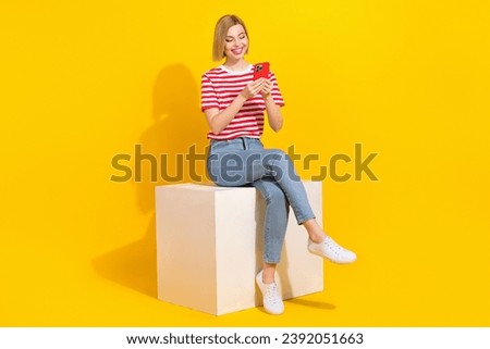 Full size portrait of lovely cheerful girl sit podium use smart phone typing blog post isolated on yellow color background
