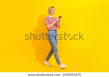 Full size profile photo of pretty positive girl walking use smart phone chatting isolated on yellow color background