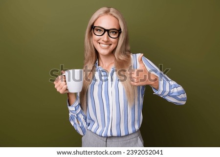 Photo portrait of blonde lovely young lady hold coffee mug thumb up wear trendy striped garment isolated on khaki color background