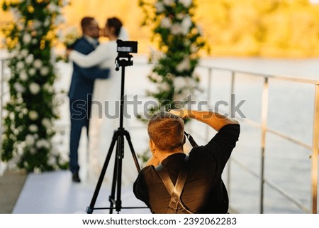 Photographer taking pictures of the bride and groom at the off-site ceremony. Selective focus. Professional videographer and wedding photographer. Royalty-Free Stock Photo #2392062283
