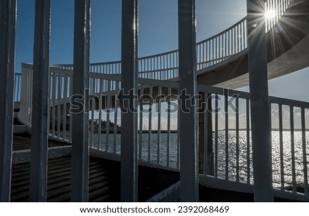 Spiral road bridge at the coast with a sunburst peeking through the railings.