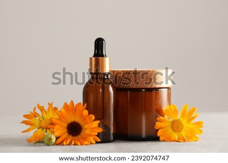 Bottle and jar of cosmetic products with beautiful calendula flowers on light grey table, closeup