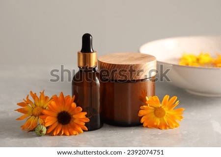 Bottle and jar of cosmetic products with beautiful calendula flowers on light grey marble table