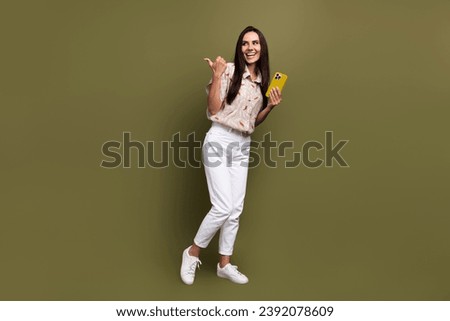 Full length shot young lady pointing finger empty space using smartphone subscribe social medias channel isolated on khaki color background