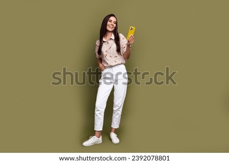 Full size body photo of attractive smiling young positive woman blogging holding mobile phone texting isolated on khaki color background