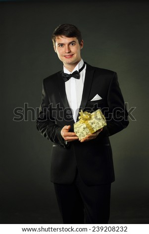 nice handsome man in a tuxedo gives a gift. On a black background.