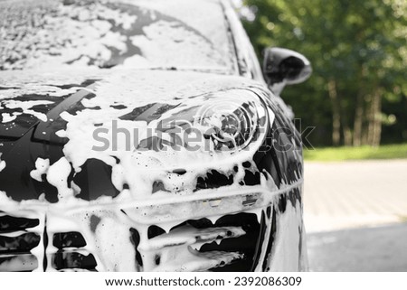 Auto covered with cleaning foam at outdoor car wash, closeup