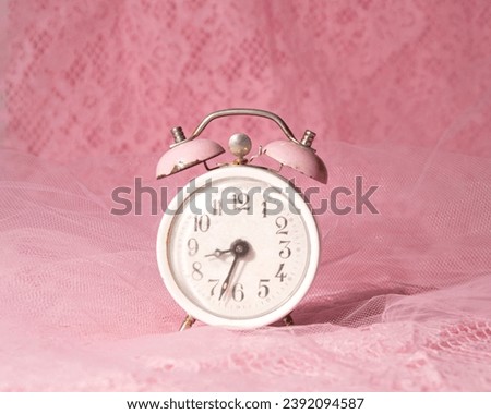 Vintage alarm clock on a pink lace background, creative aesthetic concept, morning awakening.