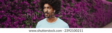 Closeup cheerful young  man listening to music in wireless headphones and dancing on background wall covered with purple flowers. Lifestyle concept.