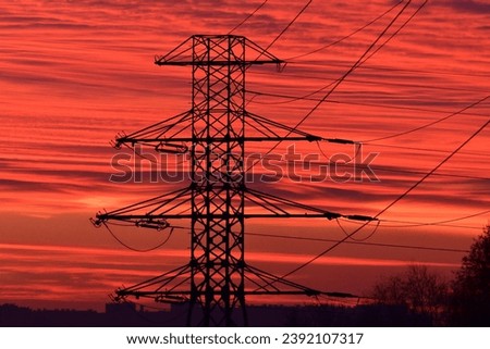 A high-voltage pole and line against the background of a burning red sky during sunrise