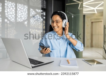 Young beautiful woman at workplace joyful listening to music and online radio, using app on phone, businesswoman resting on break, singing along well done job well done.