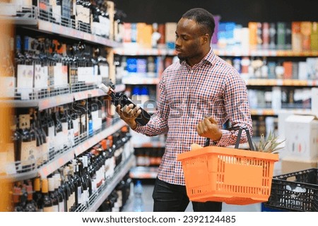 African American Man in a supermarket choosing a wine. Royalty-Free Stock Photo #2392124485