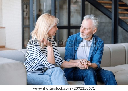 Elderly man listening carefully and try to understand woman. Sitting on sofa at home. Reliable partner. Supportive spouse. Loving, caring husband support wife