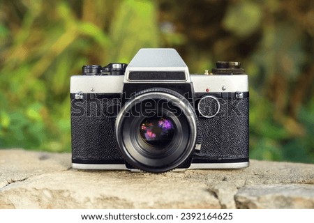 Retro film photo camera stands on a cement wall with tropical vegetation on the background outdoors