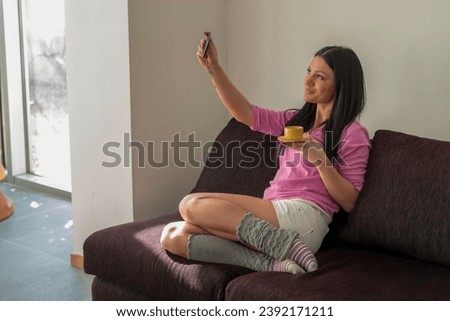 Shot of a happy young woman taking selfie with her mobile phone while sitting at living room.